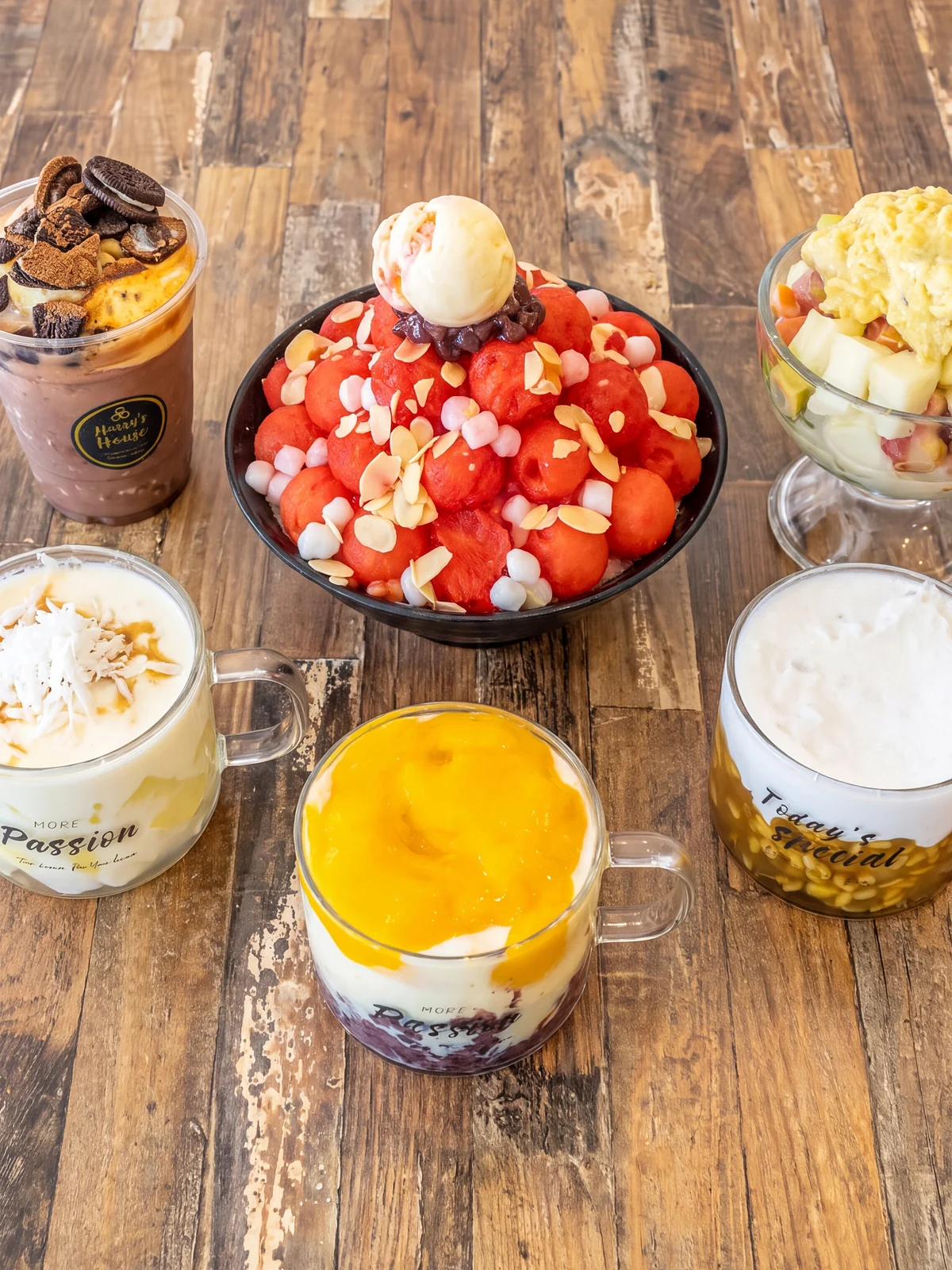 A Harry's House table from above: watermelon bingsu, purple rice yoghurt, Coco Nana, an iced chocolate and a fruit cup